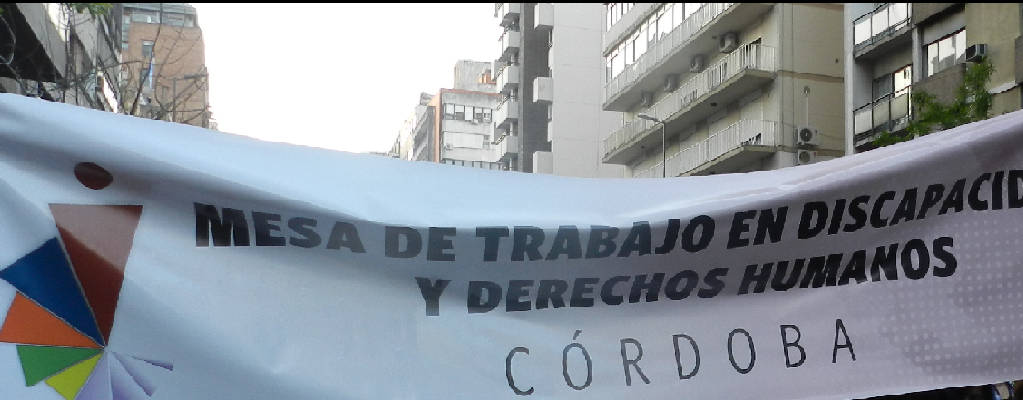 Foto sacada en marcha de salud mental. Aparece el banner con fondo blanco con el logo de la mesa. y el título : MESA DE TRABAJO EN DISCAPACIDAD Y DERECHOS HUMANOS. CÓRDOBA.